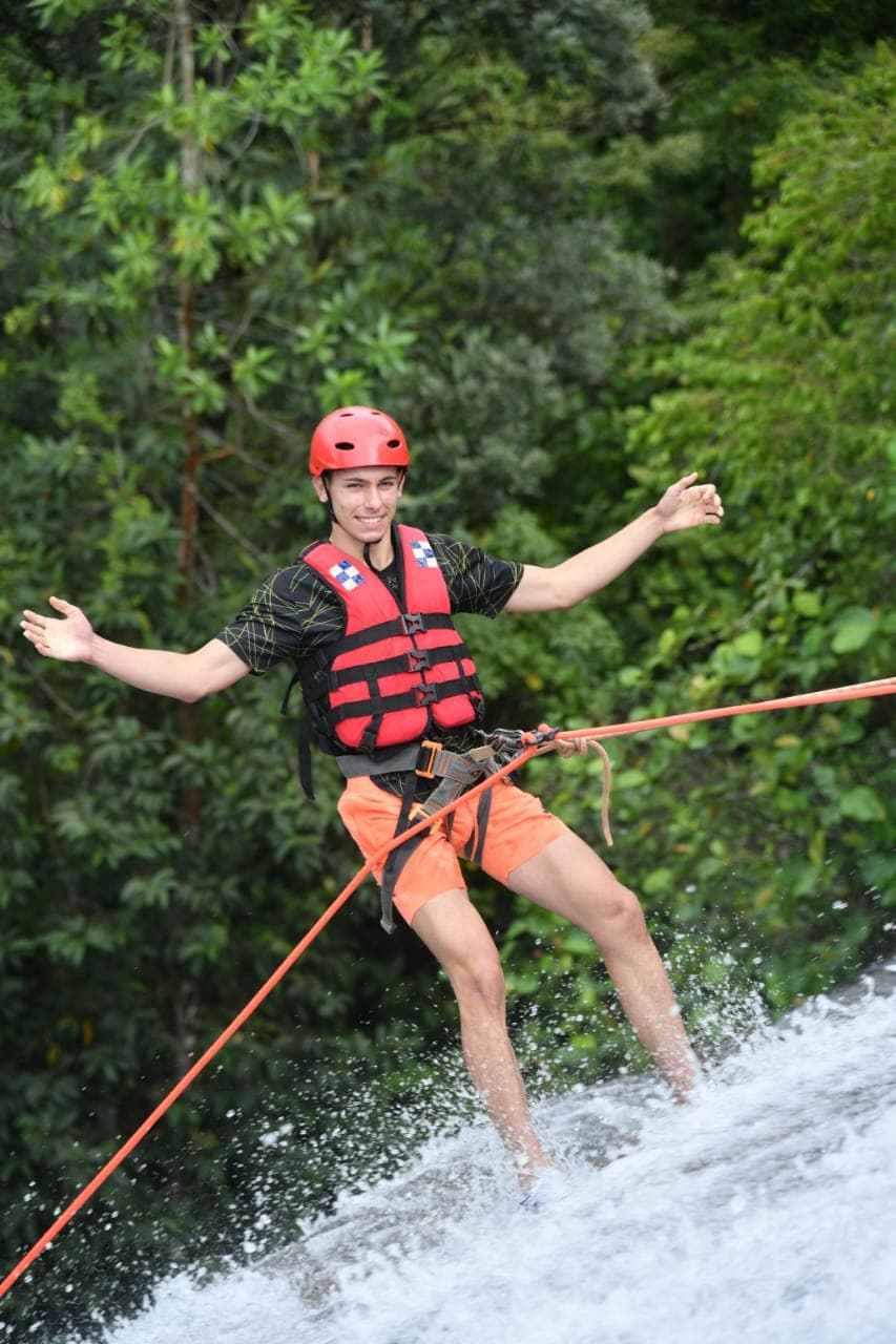 Adventurer cliff jumping into a clear rainforest waterfall pool