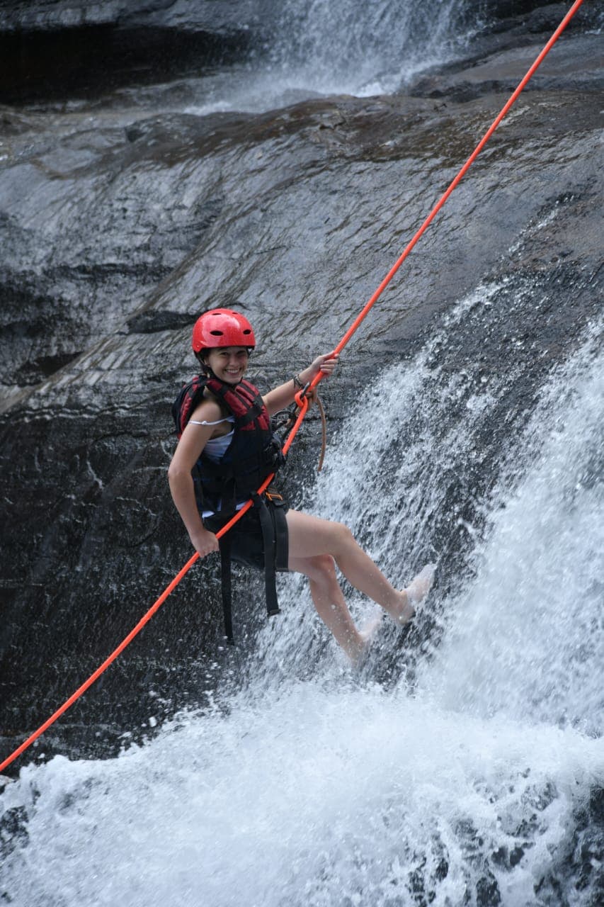 Guide assisting guest during waterfall abseiling descent
